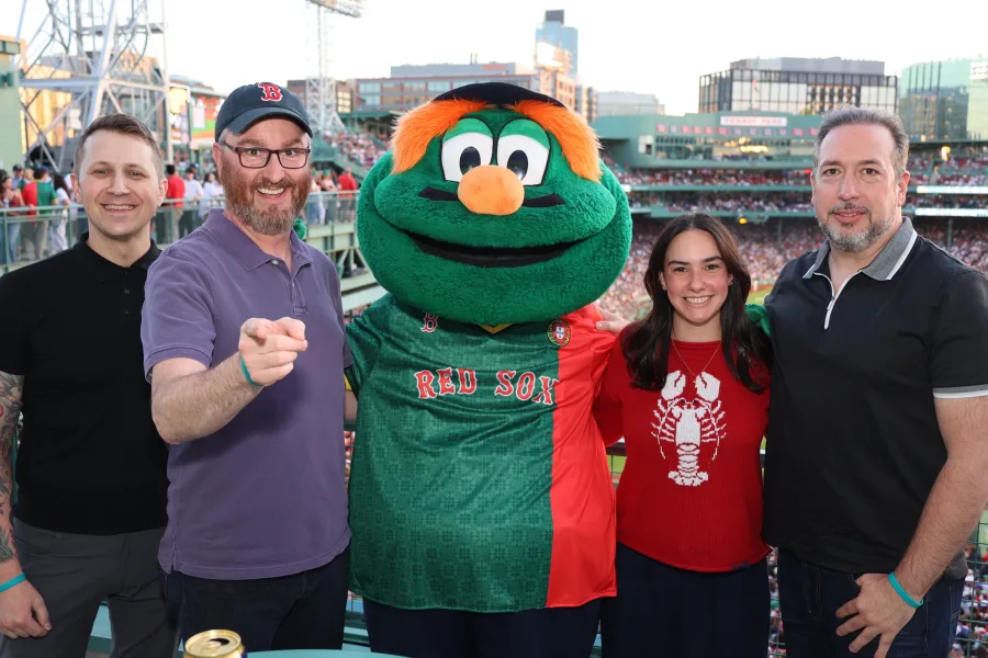 Four guests photographed with a team mascot on the concourse at a ballpark