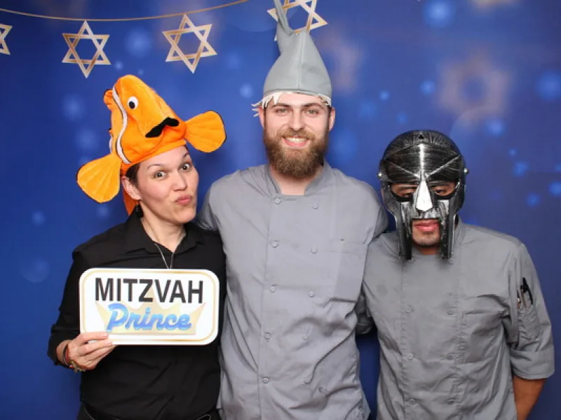 Three guests in costume hats holding a Mitzvah Prince prop sign in front of a Star of David backdrop