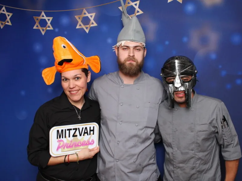 Three guests in costume hats holding a Mitzvah Princess prop sign in front of a Star of David backdrop