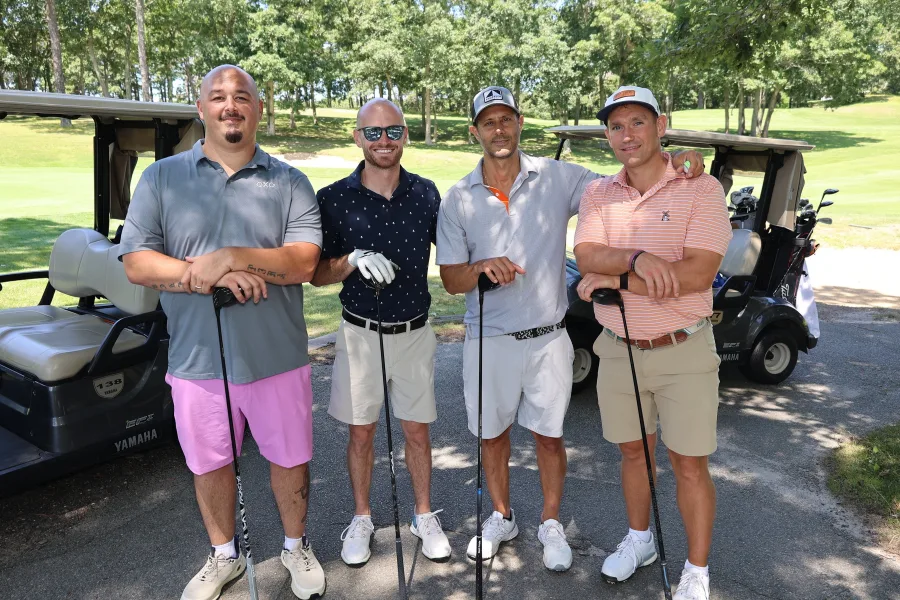 Foursome of golfers with their clubs beside the carts at a charity golf tournament