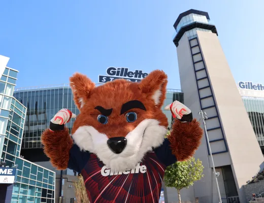 Team mascot with arms raised in front of Gillette Stadium at a gameday fan photo op