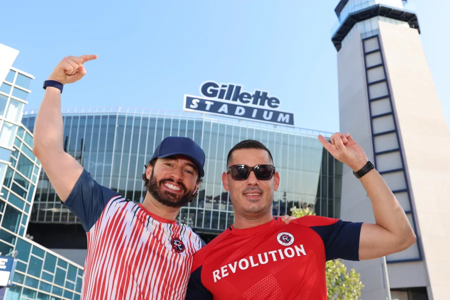 Two fans in team jerseys cheering in front of Gillette Stadium at a photo op