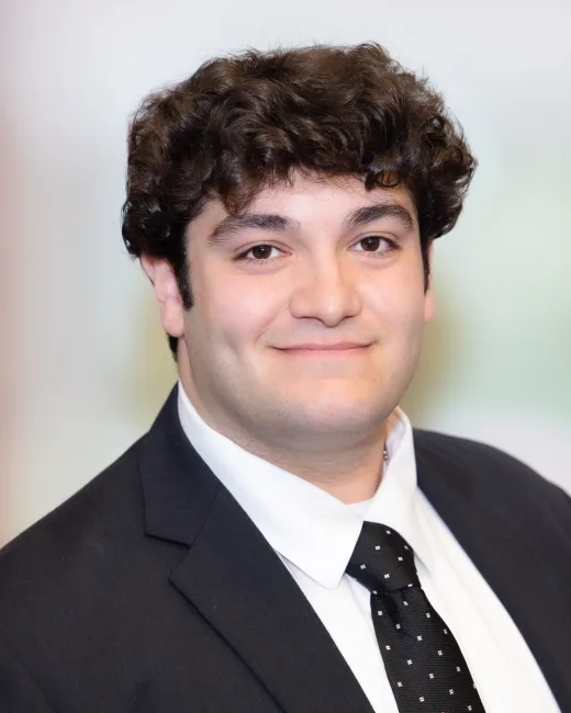 Corporate headshot of a man in a dark suit and tie on a soft neutral background