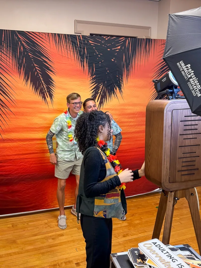 A couple posing at a tropical backdrop with the Flashback photo booth and attendant