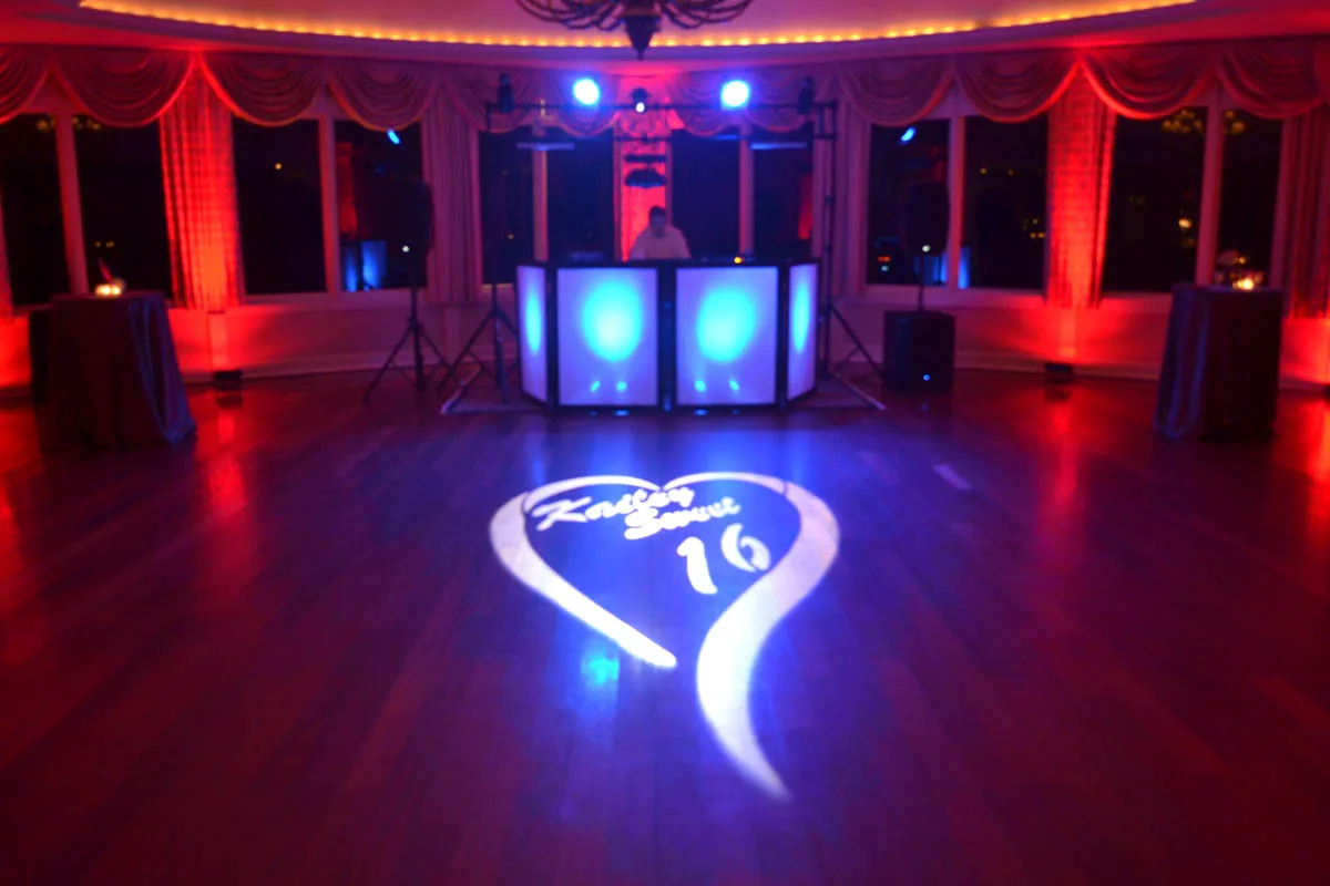 Custom heart monogram gobo projected onto a dance floor in a red-uplit ballroom