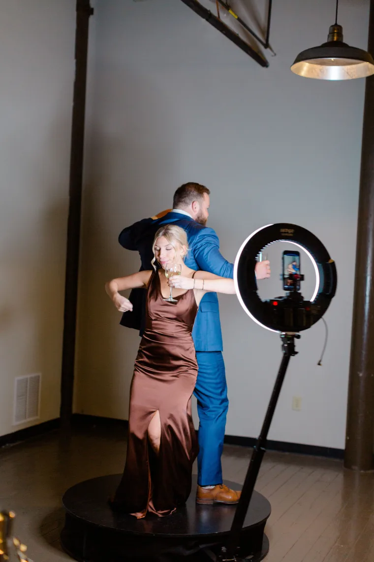 Guest posing at the 360 video booth beside the bride and groom