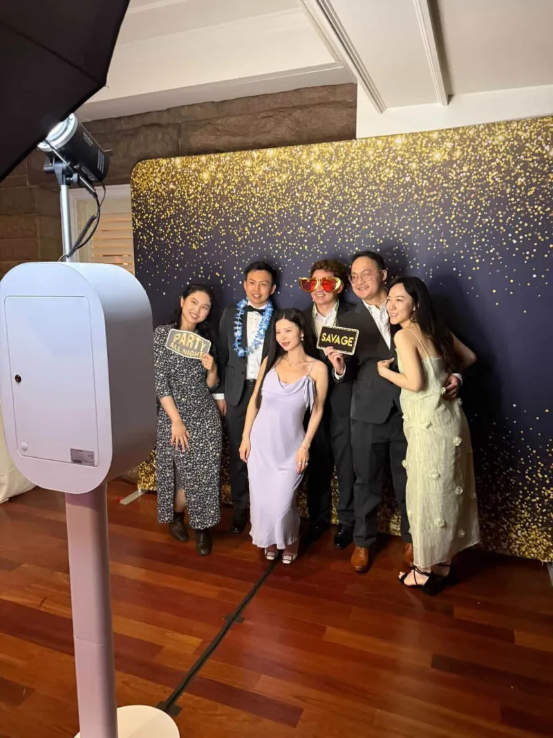 A group posing with the LuxPod photo booth in front of a gold backdrop