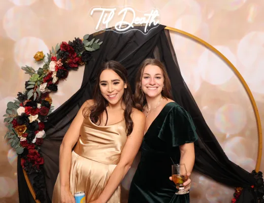 Two guests posed at a floral hoop set with a neon sign and blush backdrop