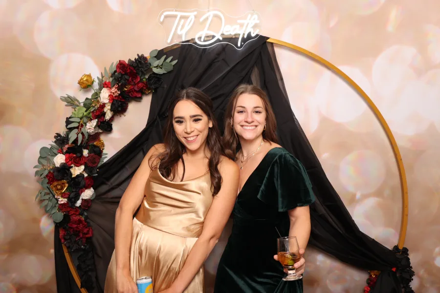Two guests posed at a floral hoop set with a neon sign and blush backdrop