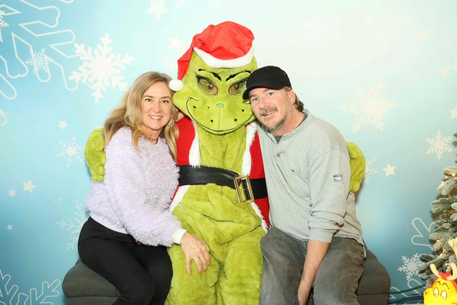 Couple posing with the Grinch beside a decorated tree at a holiday photo op