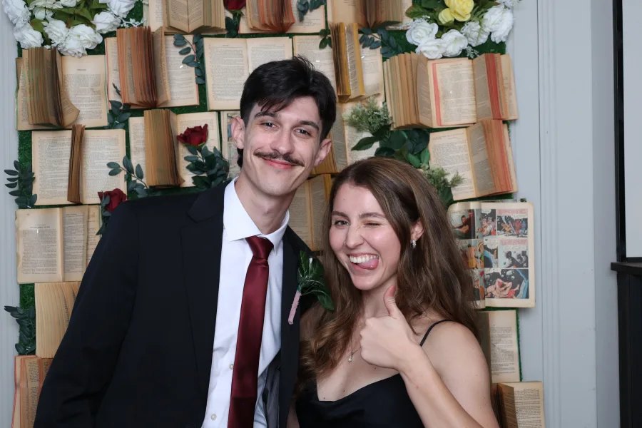 Couple photographed in front of a book page wall set with white florals