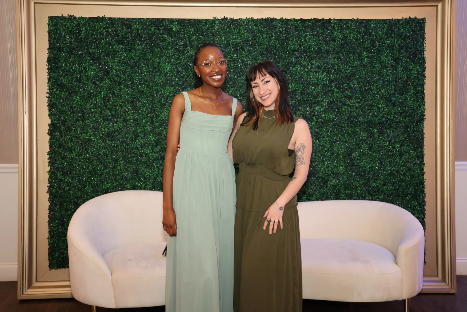 Guests photographed on white lounge sofas in front of a boxwood greenery wall at a staged photo op