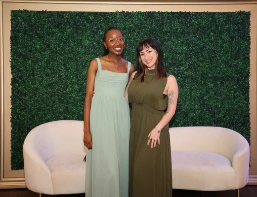 Guests photographed on white lounge sofas in front of a boxwood greenery wall