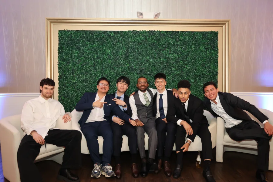 Group of guests photographed on a white sofa in front of a framed boxwood wall