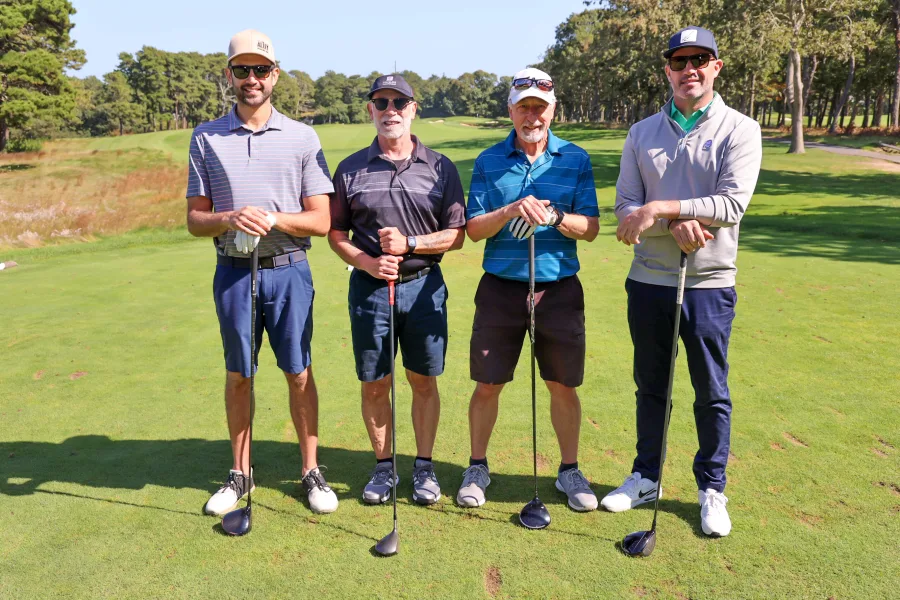 Foursome of golfers posed together on the green at a charity golf tournament