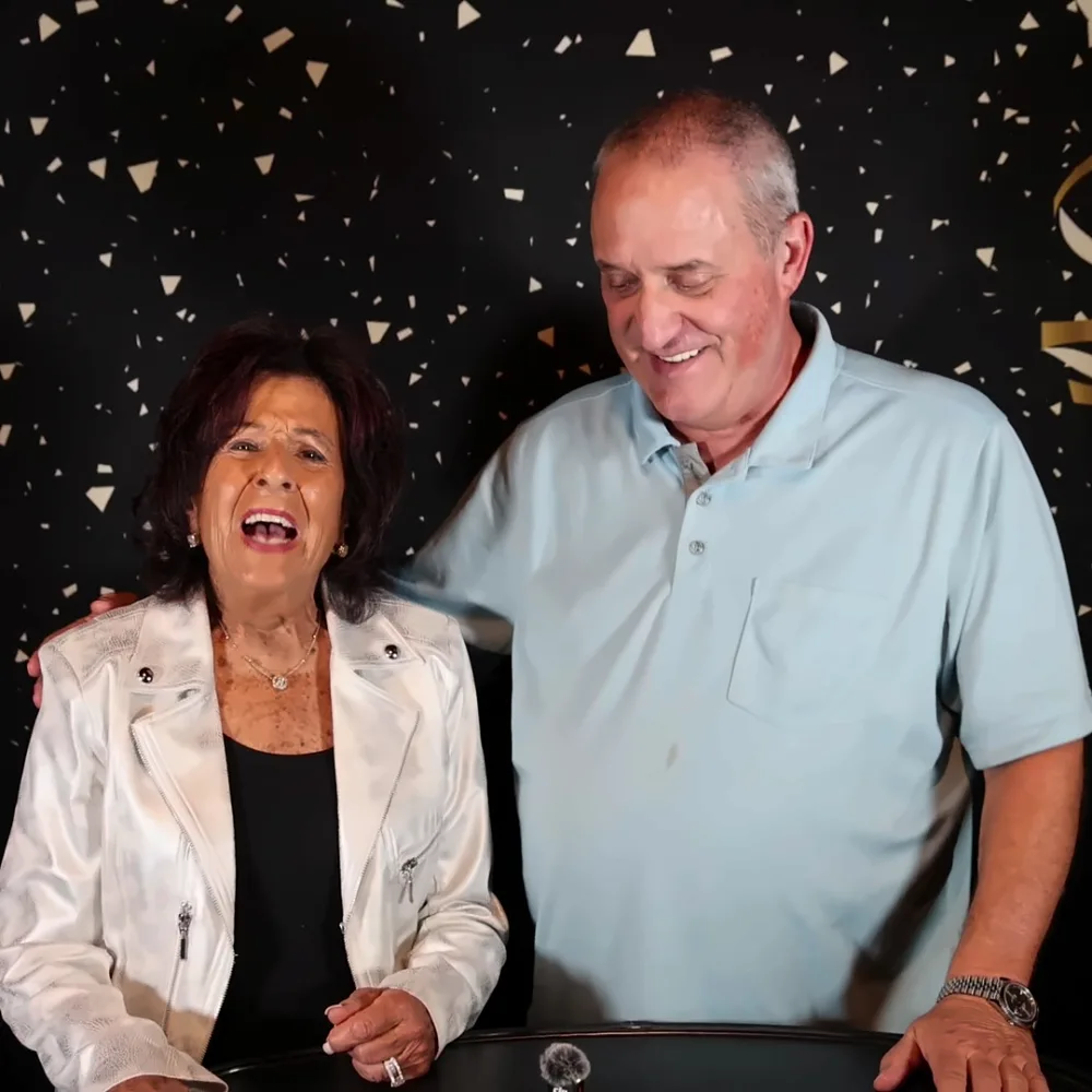 Couple laughing while recording a Confessional Booth message in front of gold streamers