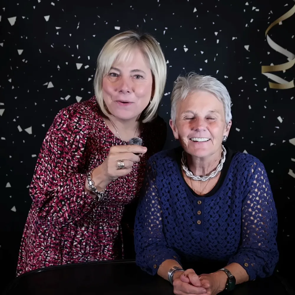 Two friends smiling while recording a Confessional Booth message at a party