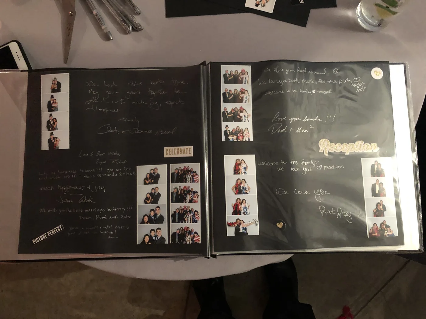 The finished guest book open on a reception table, both pages filled with photo strips and handwritten notes
