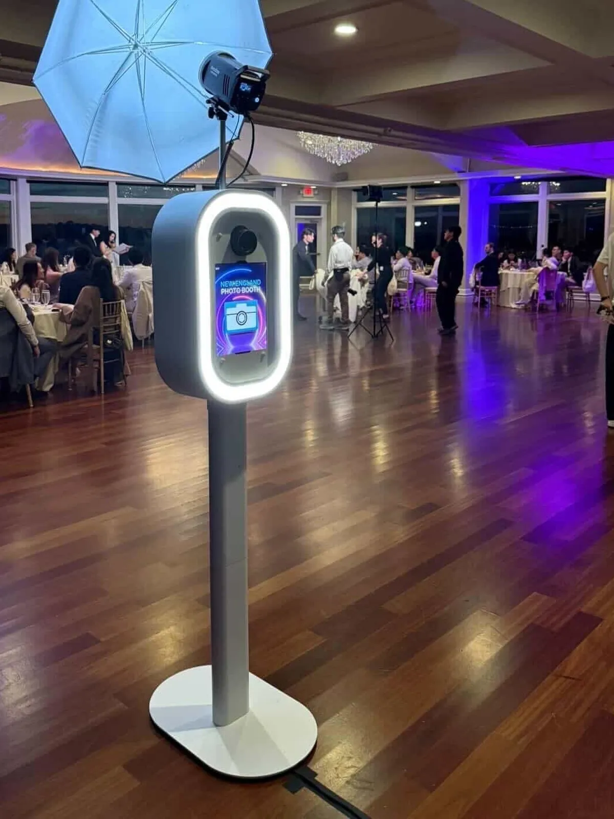 LuxPod photo booth with its LED ring light glowing on a reception dance floor lit in purple