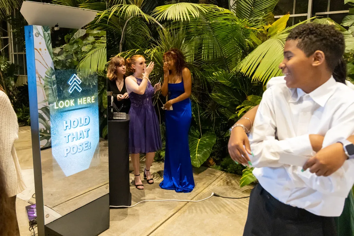 Guests in formal dresses posing at the Mirror photo booth at a garden venue