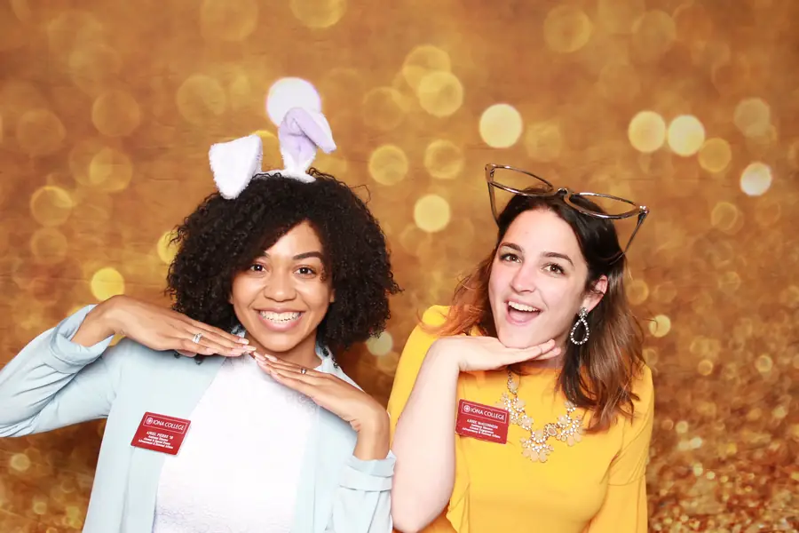Two guests laughing in the photo booth against a gold sparkle backdrop
