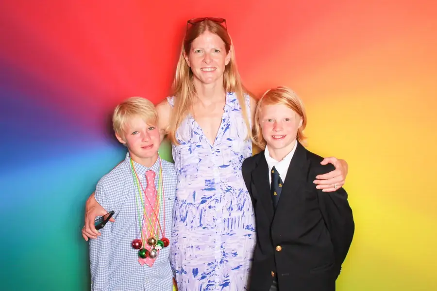 A parent and two children in the photo booth against a rainbow backdrop