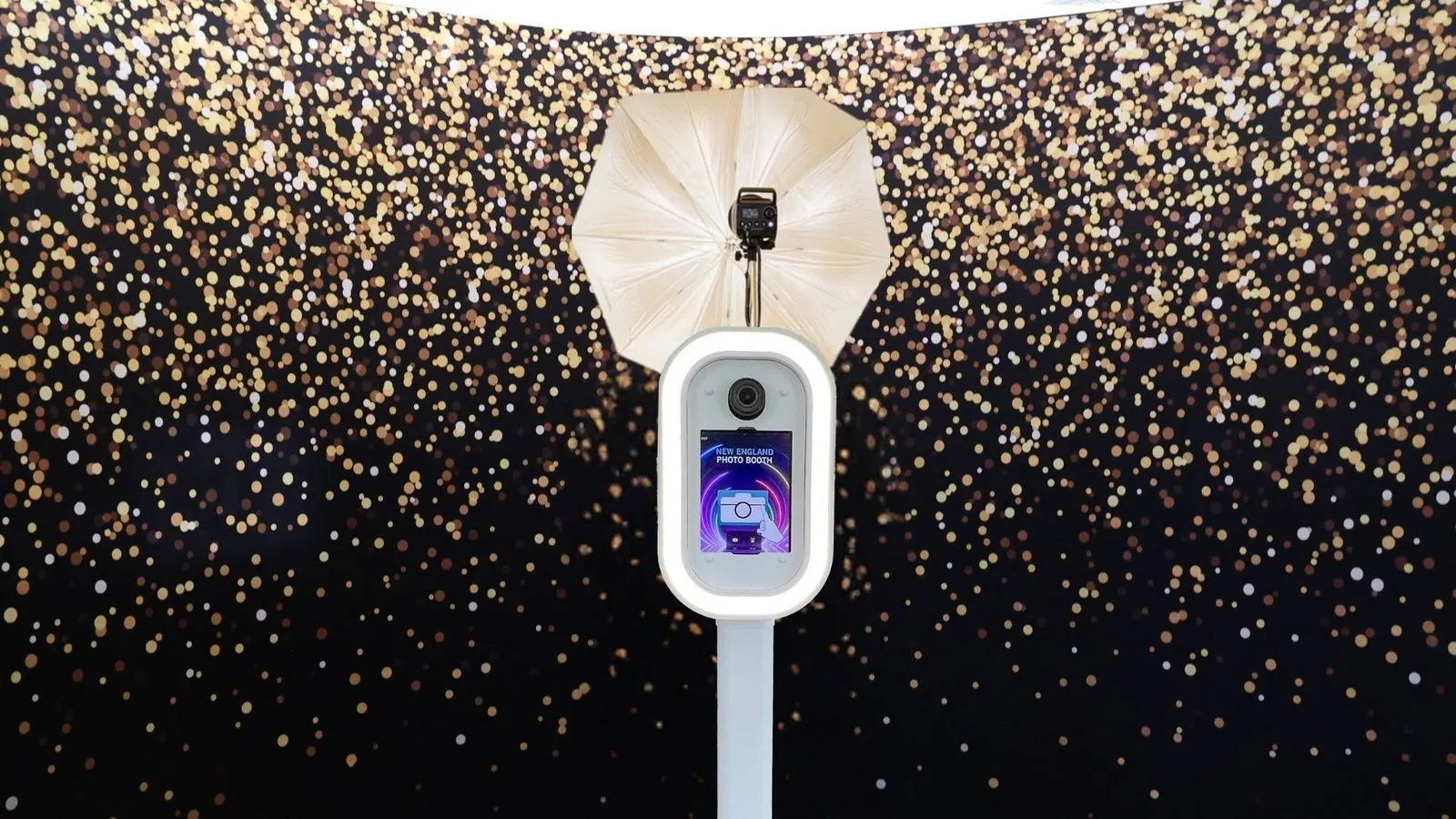 LuxPod photo booth with its LED ring light lit, in front of a gold-confetti backdrop