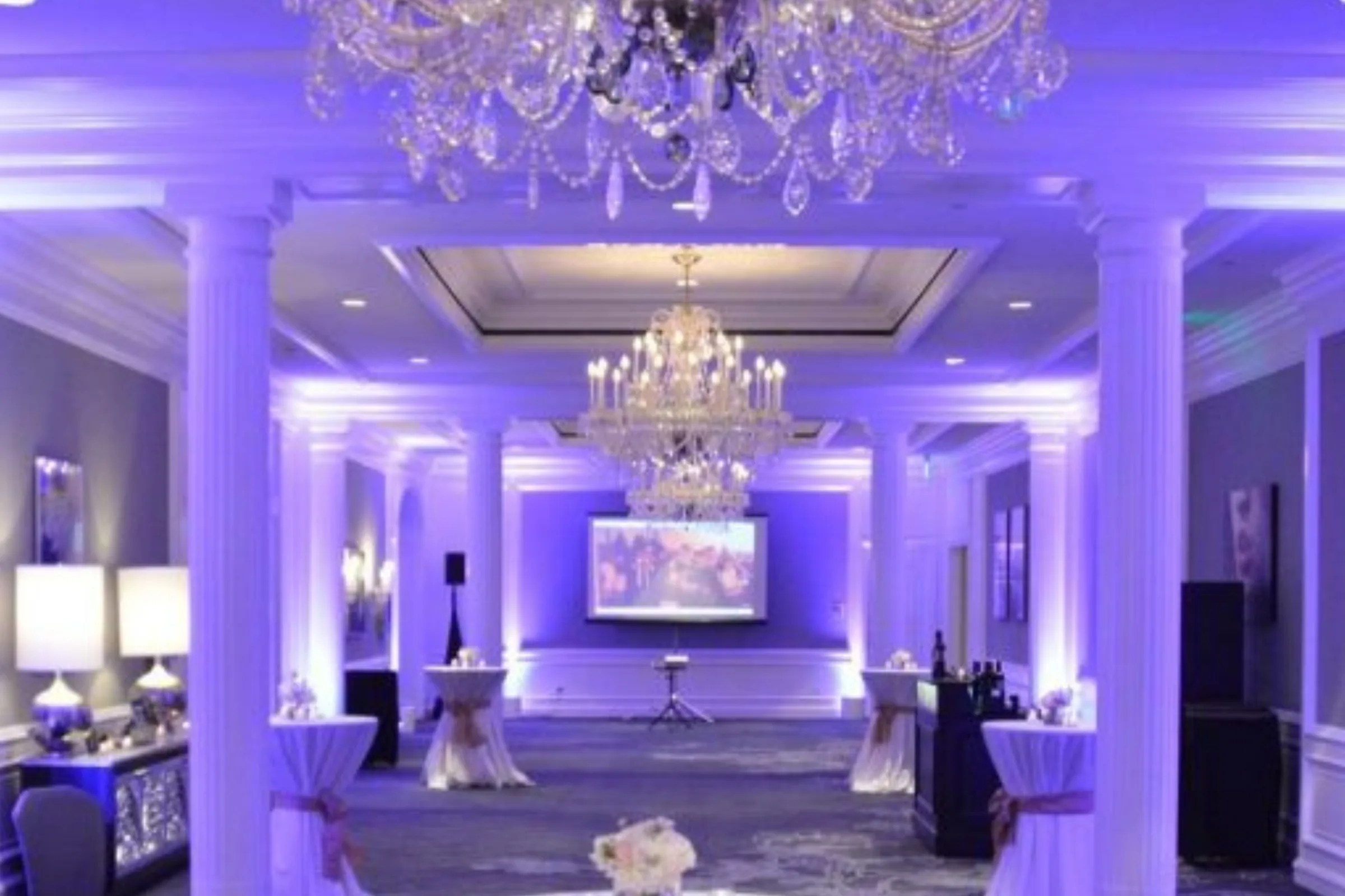 Ballroom washed in purple LED uplighting, columns and crystal chandeliers lit from the floor