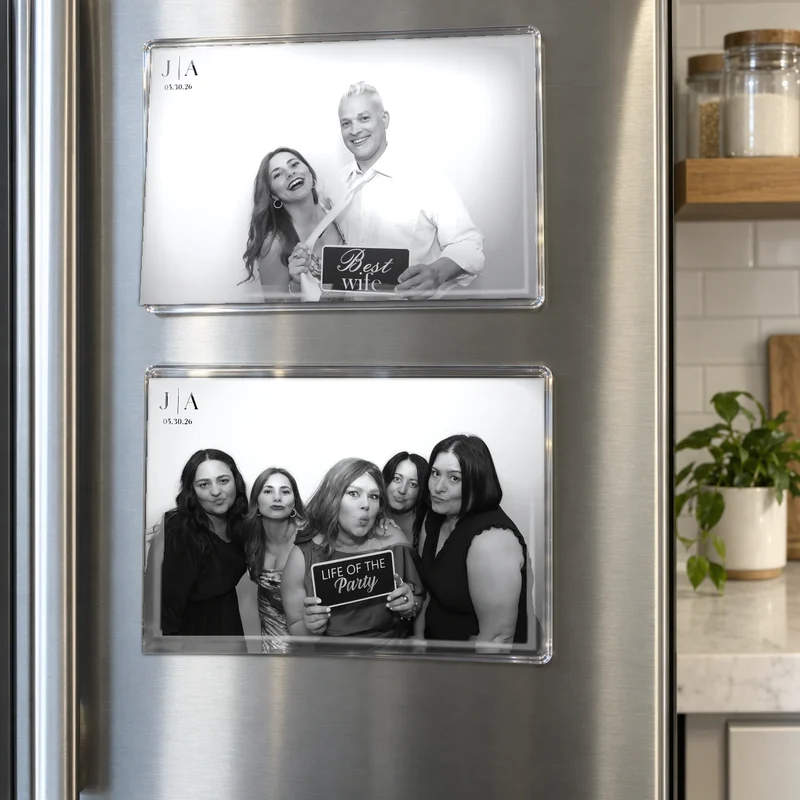 Two 4×6 photo booth prints in clear acrylic magnet frames on a stainless fridge